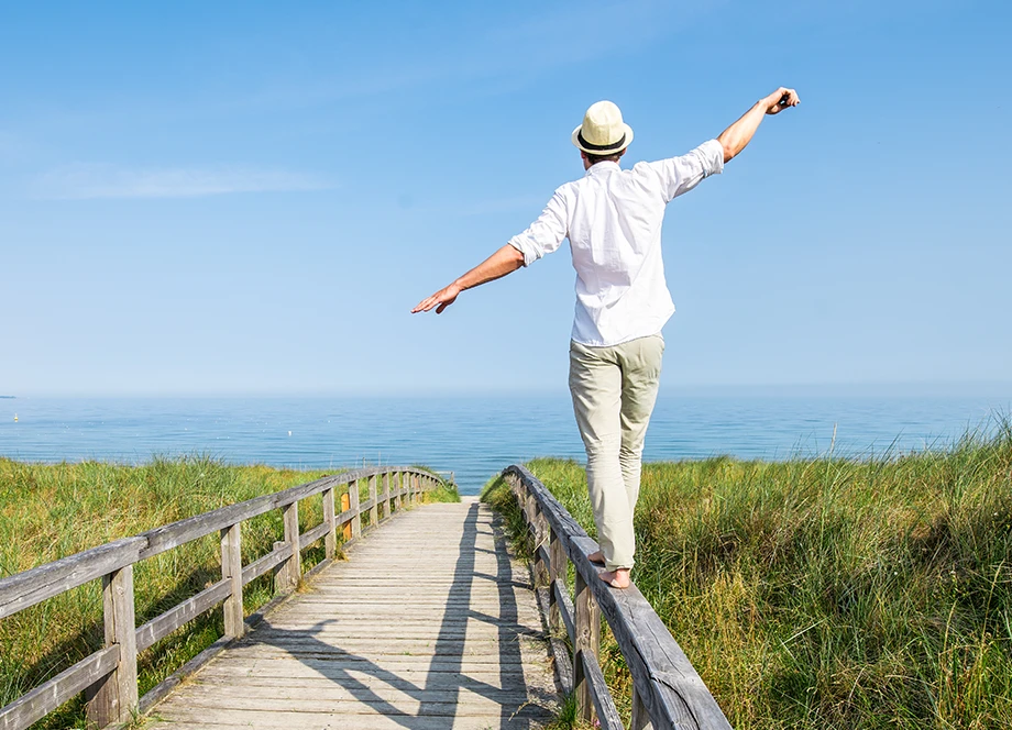Mann mit Hut in sommerlicher Kleidung balanciert barfuß über ein Holzgeländer am Stand